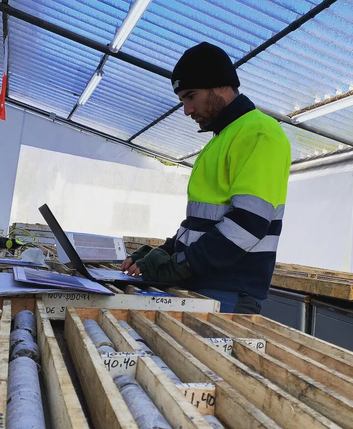 Geologist with a laptop logging drill core in boxes under a translucent roof