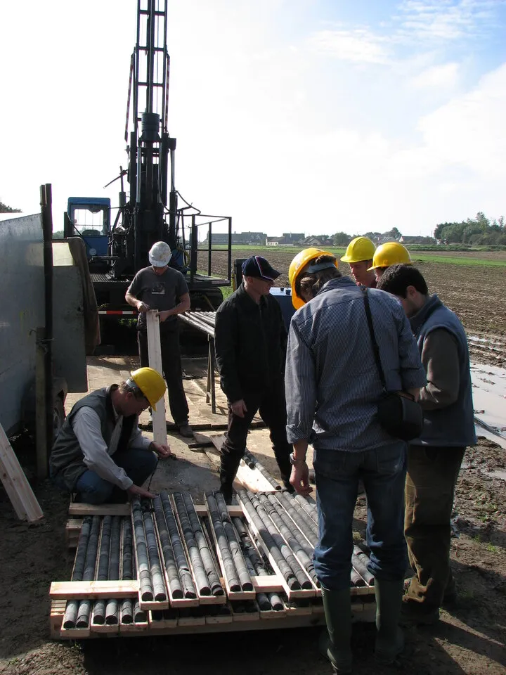 Field crew in hard hats inspecting drill core trays beside a drilling rig