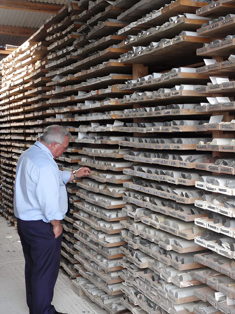 Man standing beside racks of drill core boxes in a core shed