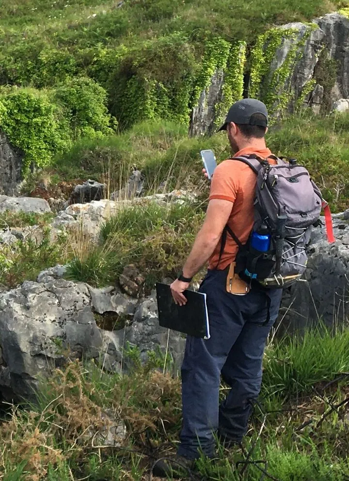Geologist with a backpack and field notebook on a grassy limestone slope