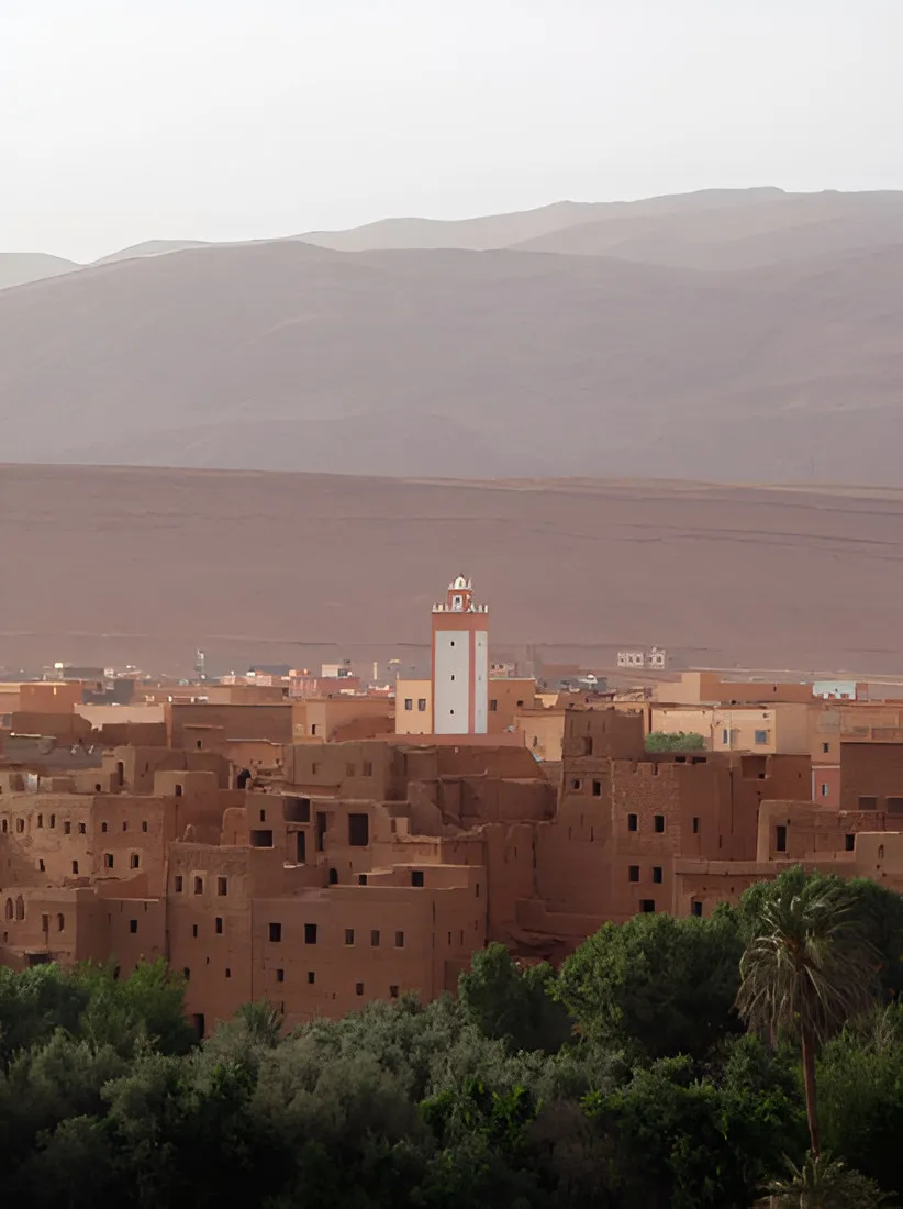Town of red earthen buildings with a minaret below arid mountains