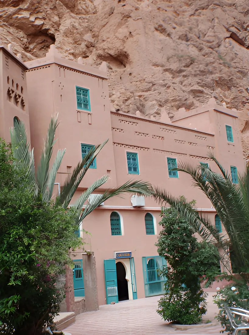 Pink kasbah-style building with turquoise shutters beneath a cliff