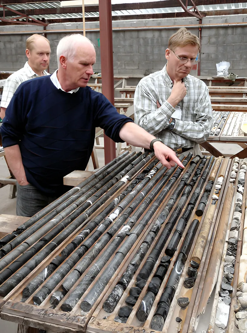 Three men examining drill core laid out in trays