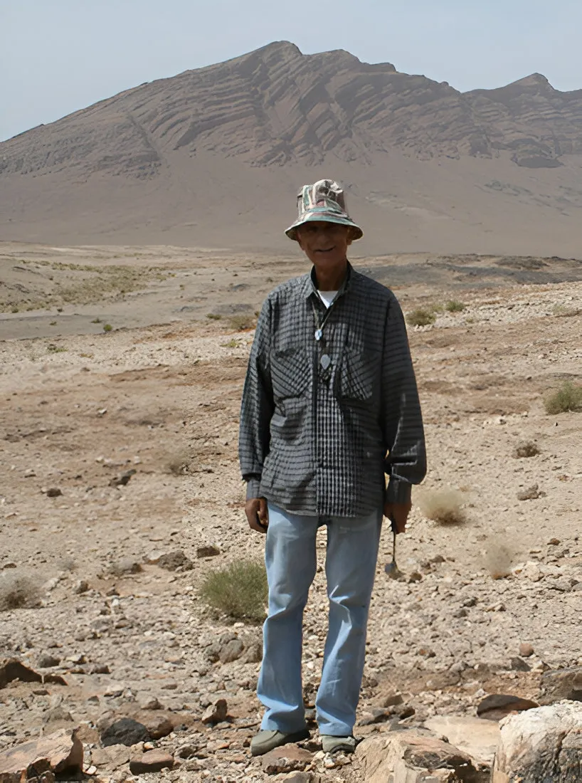 Man in a sun hat standing in a stony desert with a mountain behind