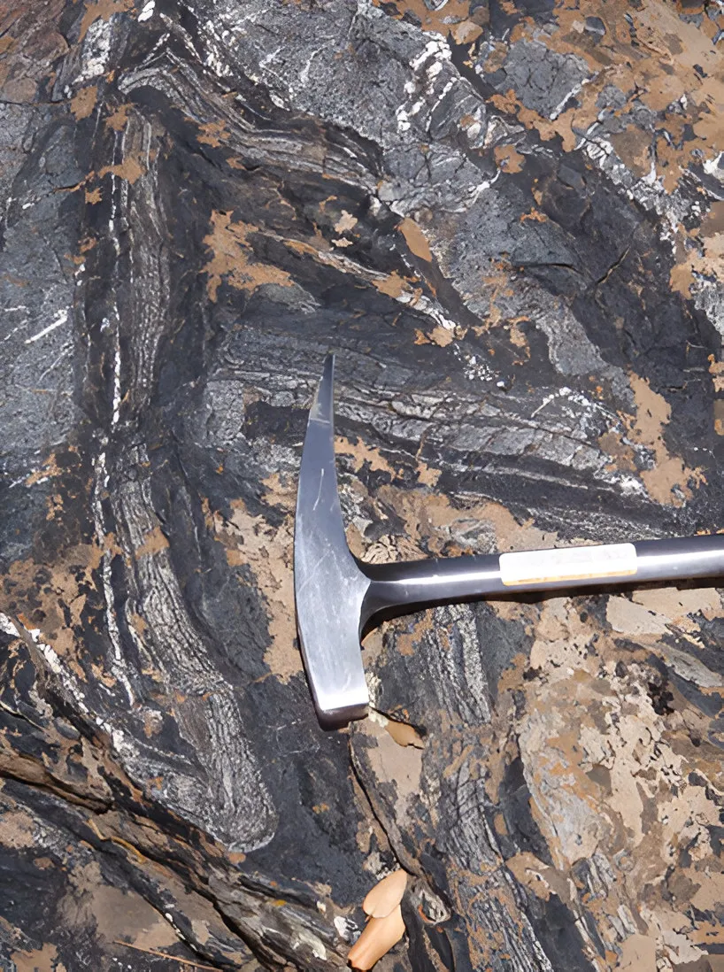 Banded tourmalinised rock with a geological hammer, Achmmach, Morocco